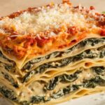 A serving of creamy spinach mushroom lasagna with layers of spinach, mushrooms, and creamy white sauce topped with melted cheese.