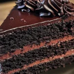 A slice of moist Black Velvet Cake with cream cheese frosting and edible gold leaf garnish.
