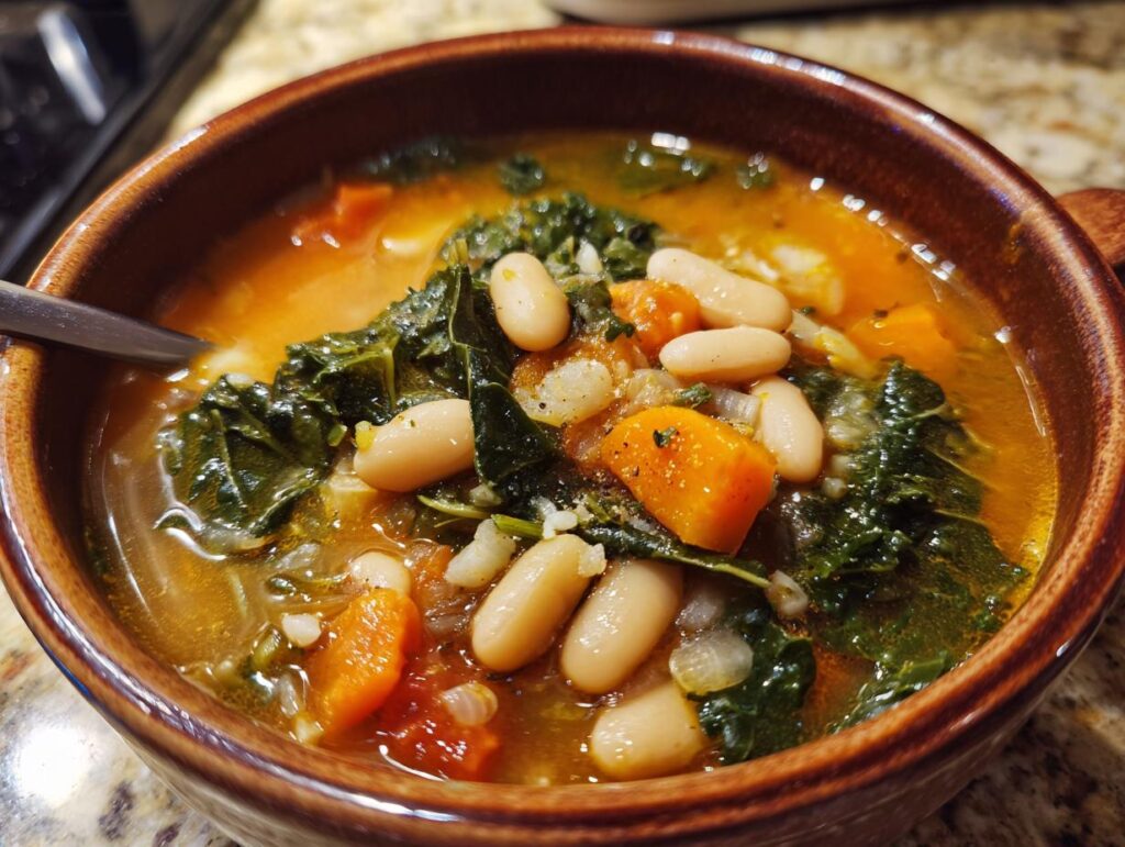 Close-up of a bowl of Tuscan White Bean & Kale Soup with beans, kale, and carrots.