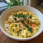 Close-up of a bowl of creamy chicken tortellini soup with chicken, tortellini, and carrots.