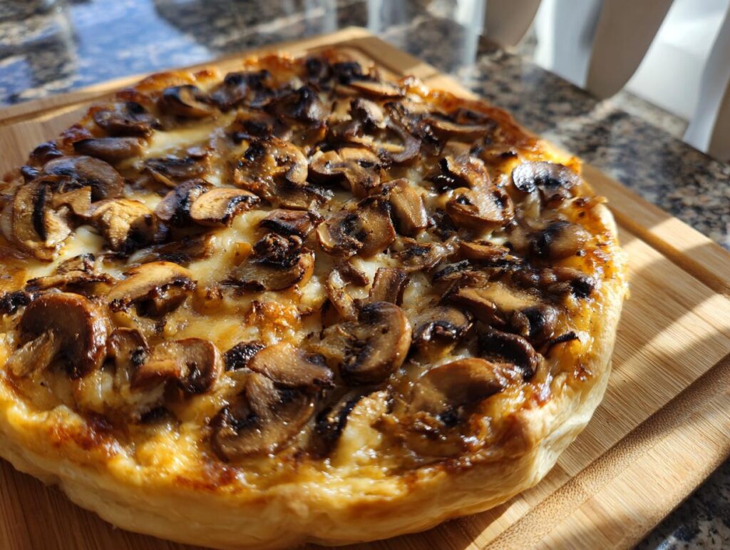 Close-up of a golden Mushroom & Gruyere Tart on a wooden board.